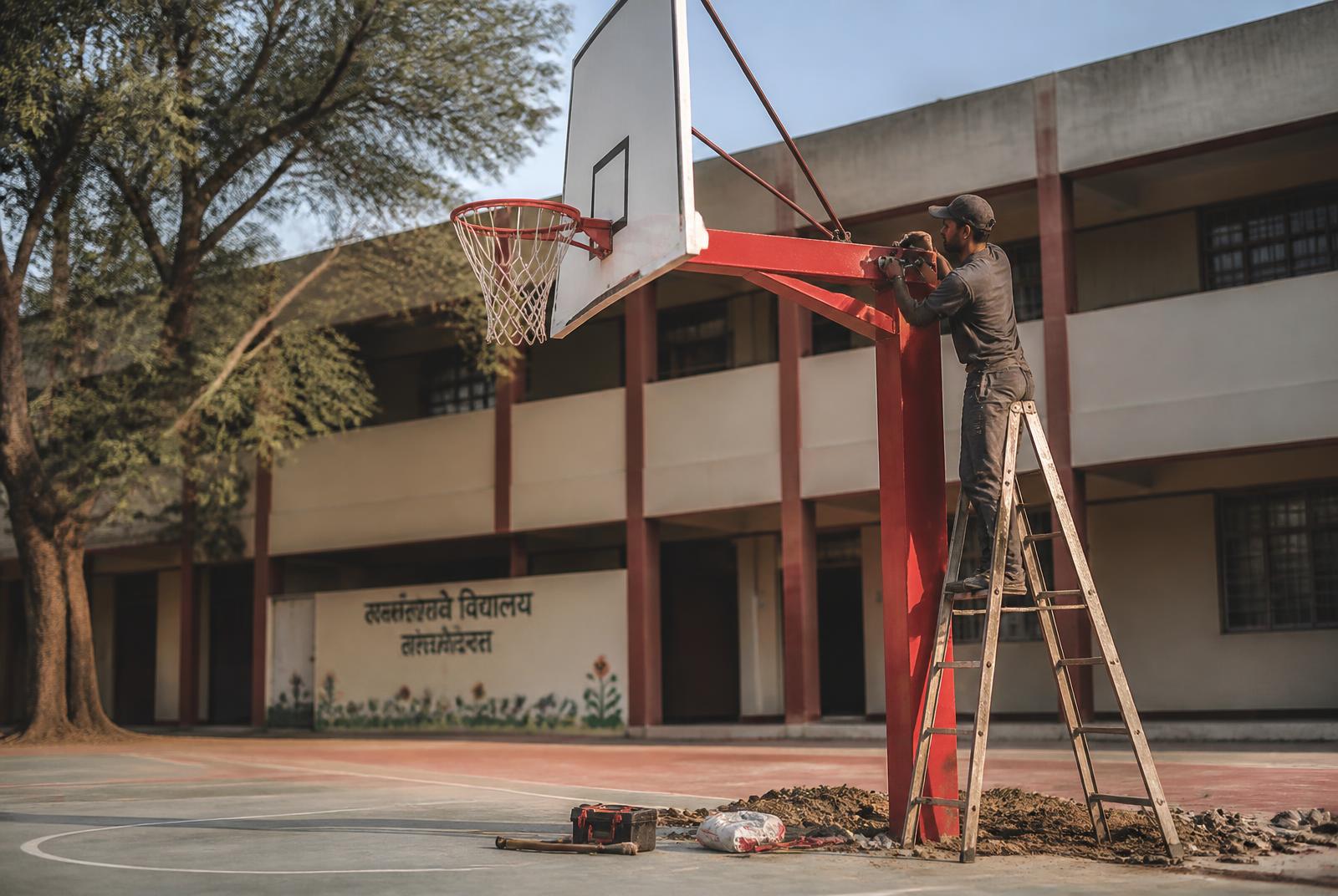 Technician installing a steel basketball post on a school court